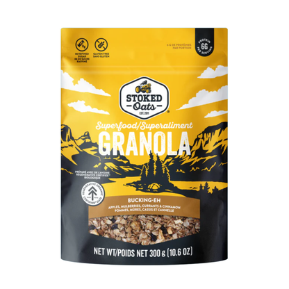 A bowl of Stoked Oats granola blend with oats, nuts, and dried fruit in a clear glass dish on a wooden surface.